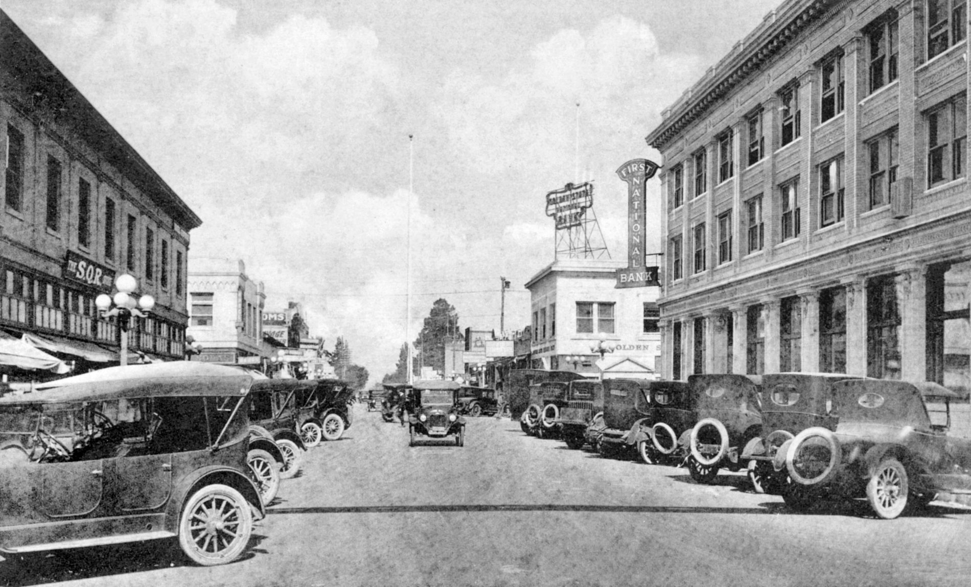 Historic photograph of Los Angeles Street in downtown Anaheim, lined with early motor cars and dominated by the First National Bank building.